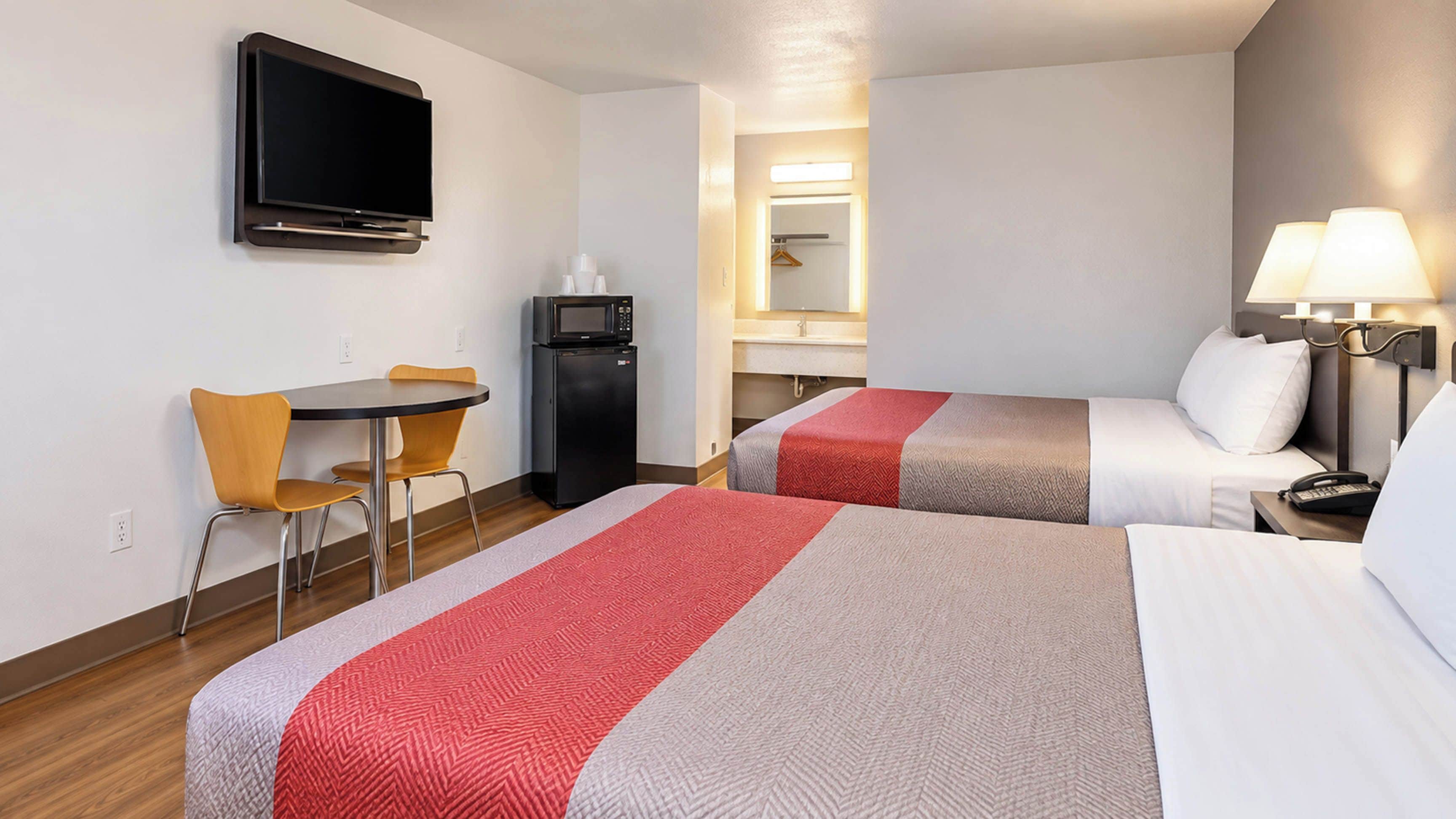 Een hotelkamer met twee bedden, een bureau met stoel, een televisie, een magnetron en een spiegel.