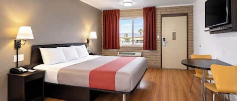 Una habitación de hotel con cama, lámparas de noche, escritorio, silla, televisor y ventana con cortinas.