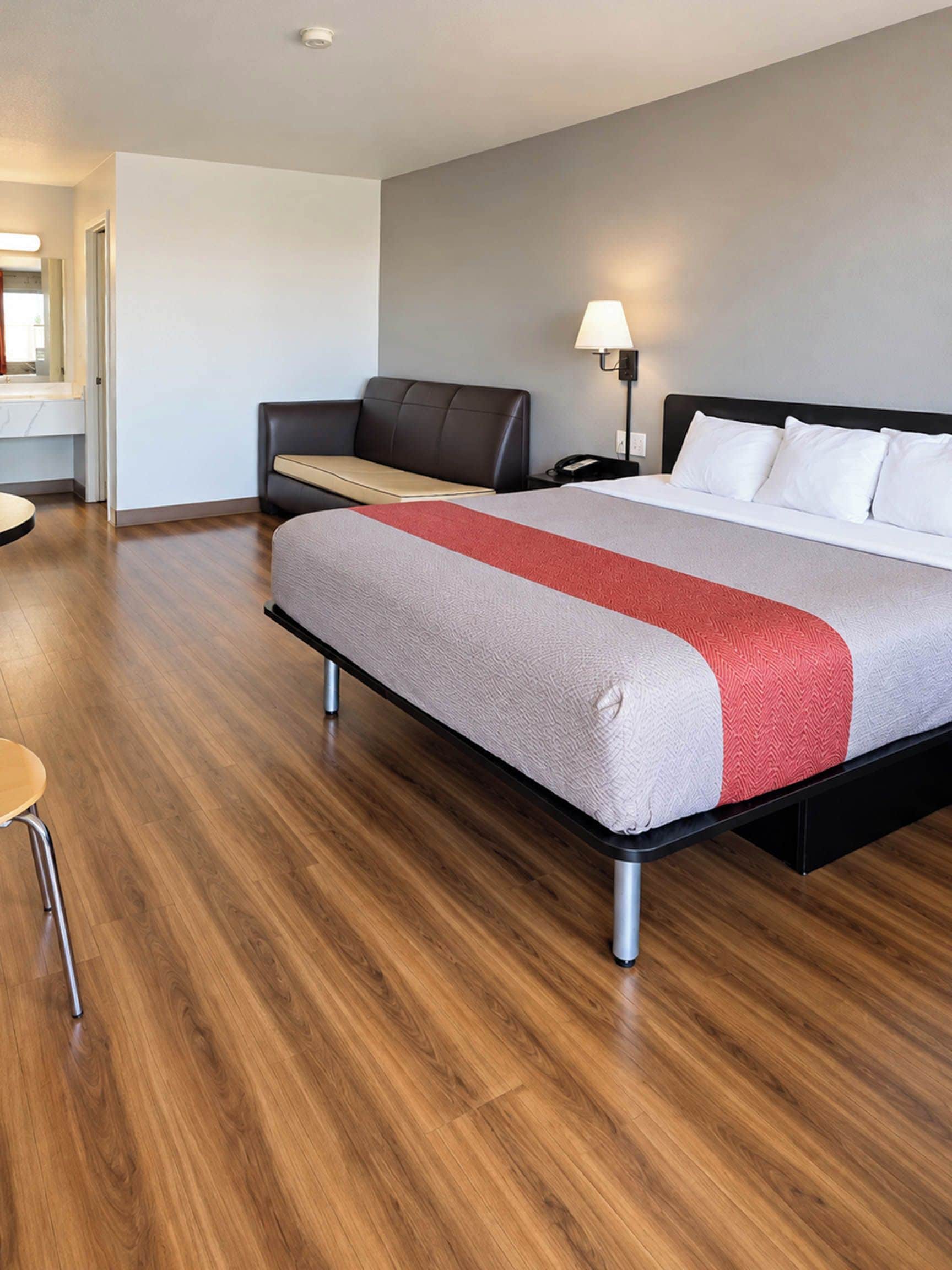 A hotel room with a bed, a desk, a chair, and a lamp.