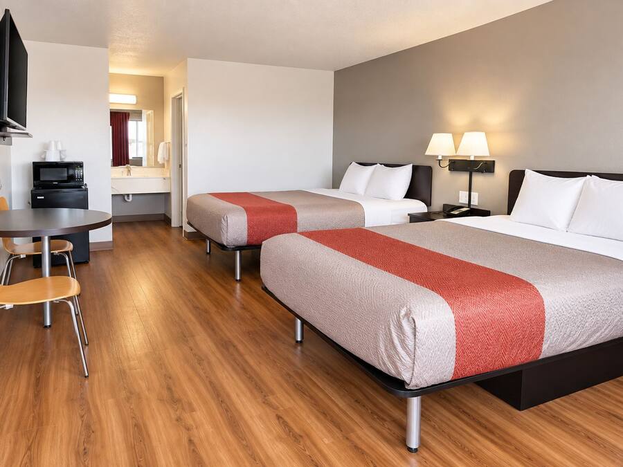 Habitación de hotel con dos camas, un escritorio, una silla, un televisor, un microondas y una lámpara.