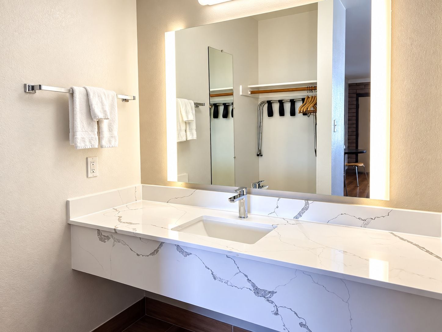 A modern bathroom with a white marble sink, a large mirror, and a towel rack.