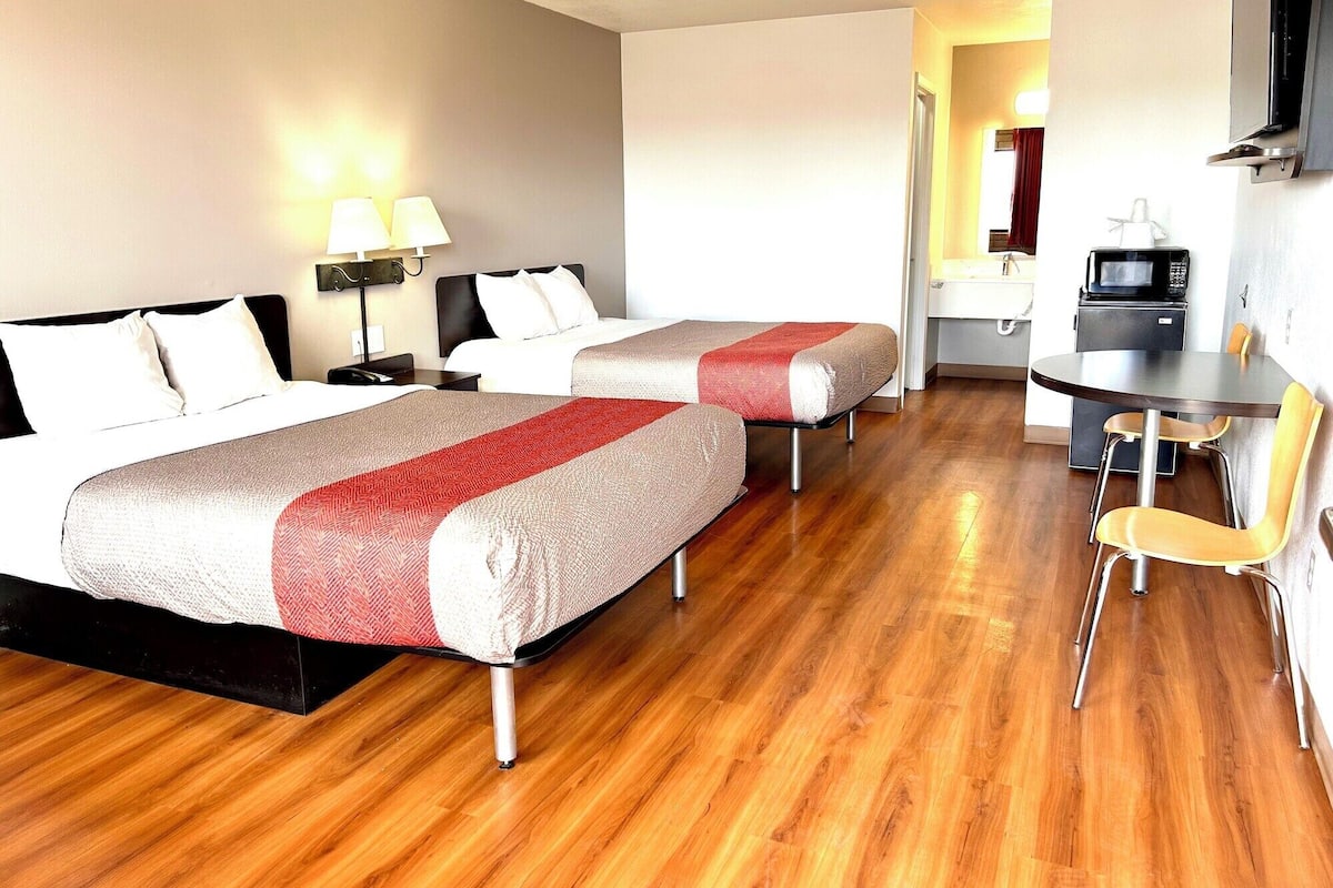 A hotel room with two beds, a desk with a chair, a microwave, and a TV.
