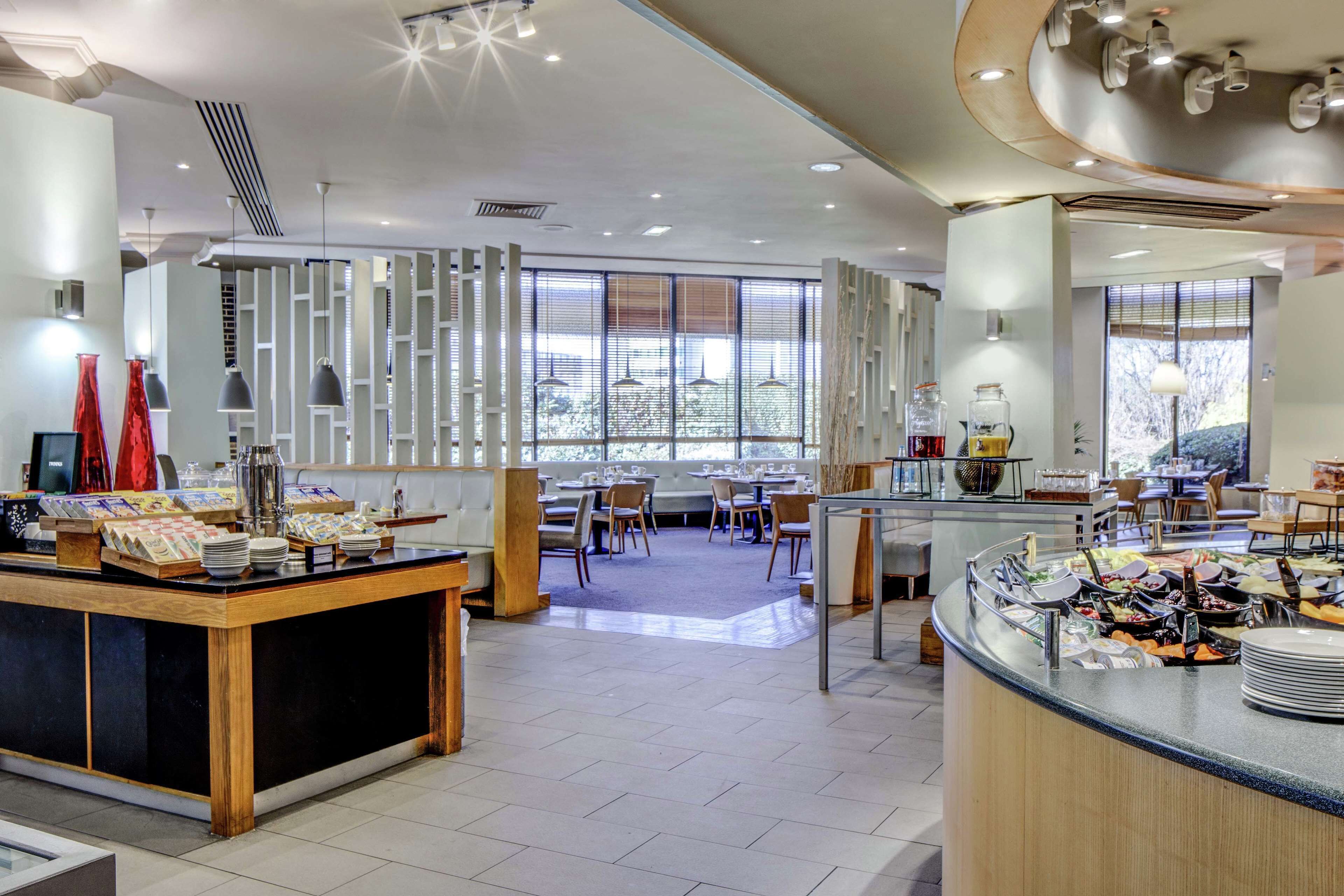 Un moderno hall de hotel con zona de buffet, arreglos de asientos y grandes ventanales que permiten la entrada de luz natural.