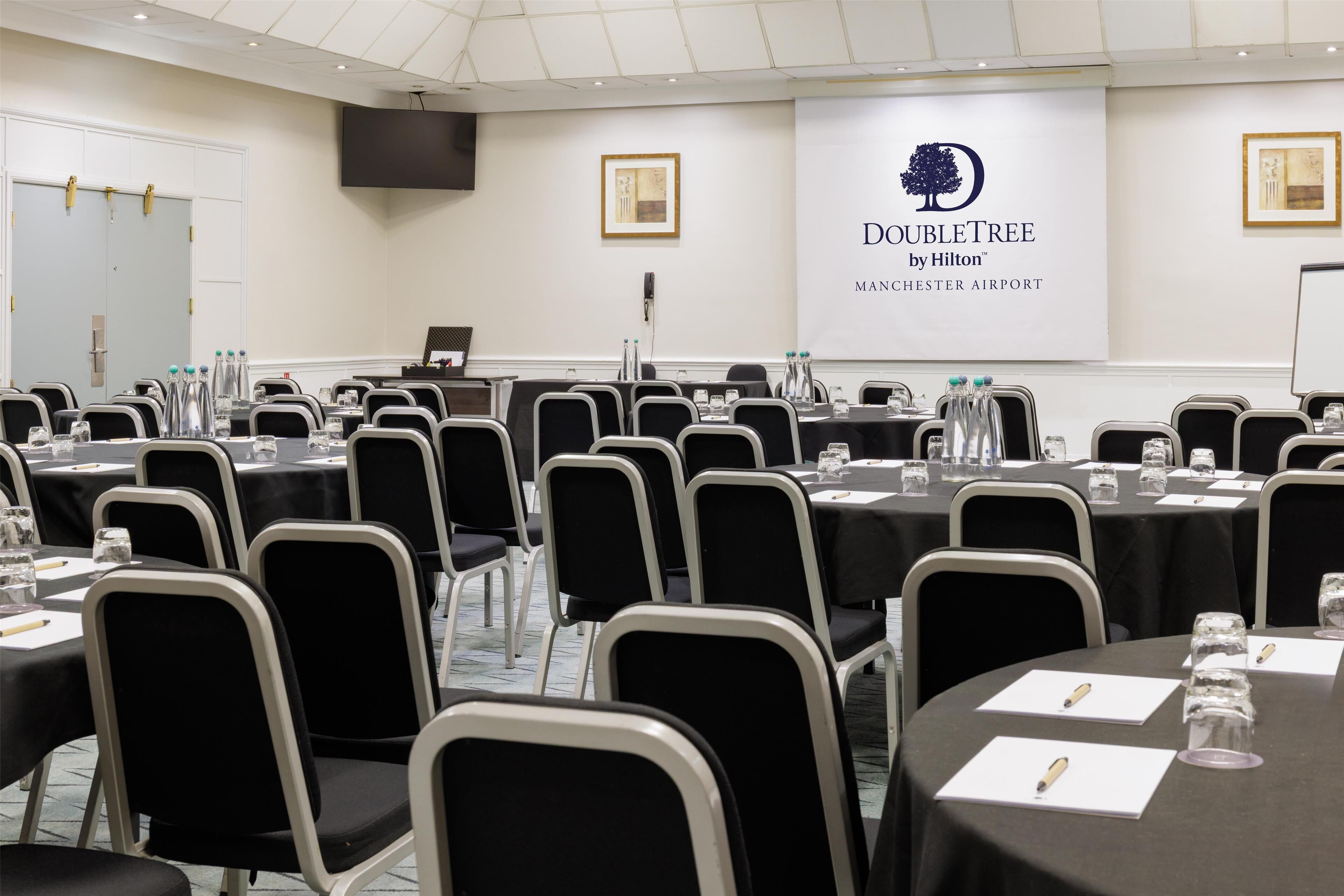 A conference room with tables and chairs, a podium, and a banner with the DoubleTree logo.