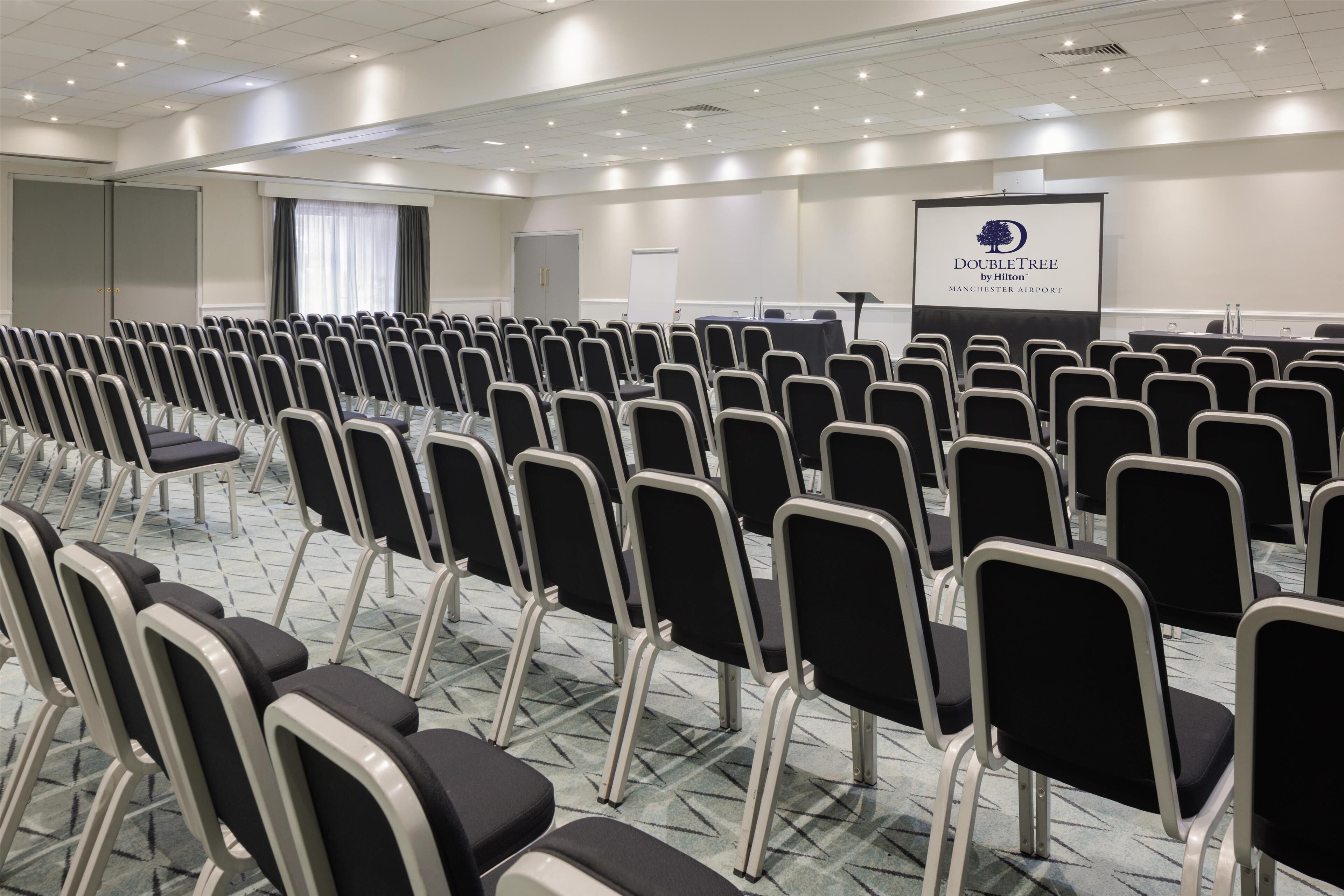 A conference room with rows of chairs, a presentation screen, and a carpeted floor.