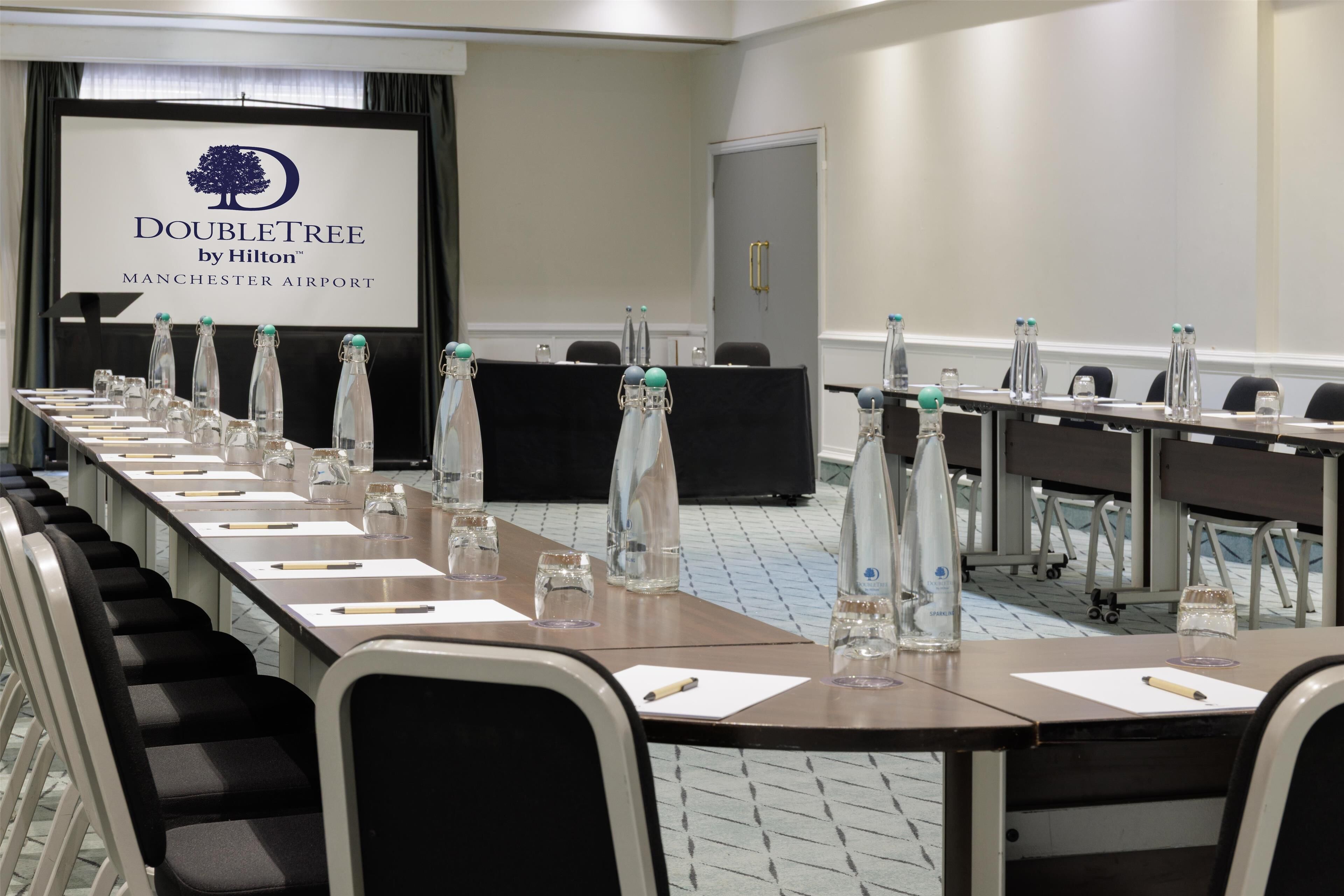 A conference room with a long table, chairs, and a screen displaying the DoubleTree by Hilton logo.