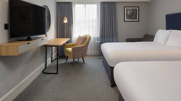 Habitación de hotel con televisión de pantalla plana, un escritorio pequeño, una silla, una cama y una ventana con cortinas.