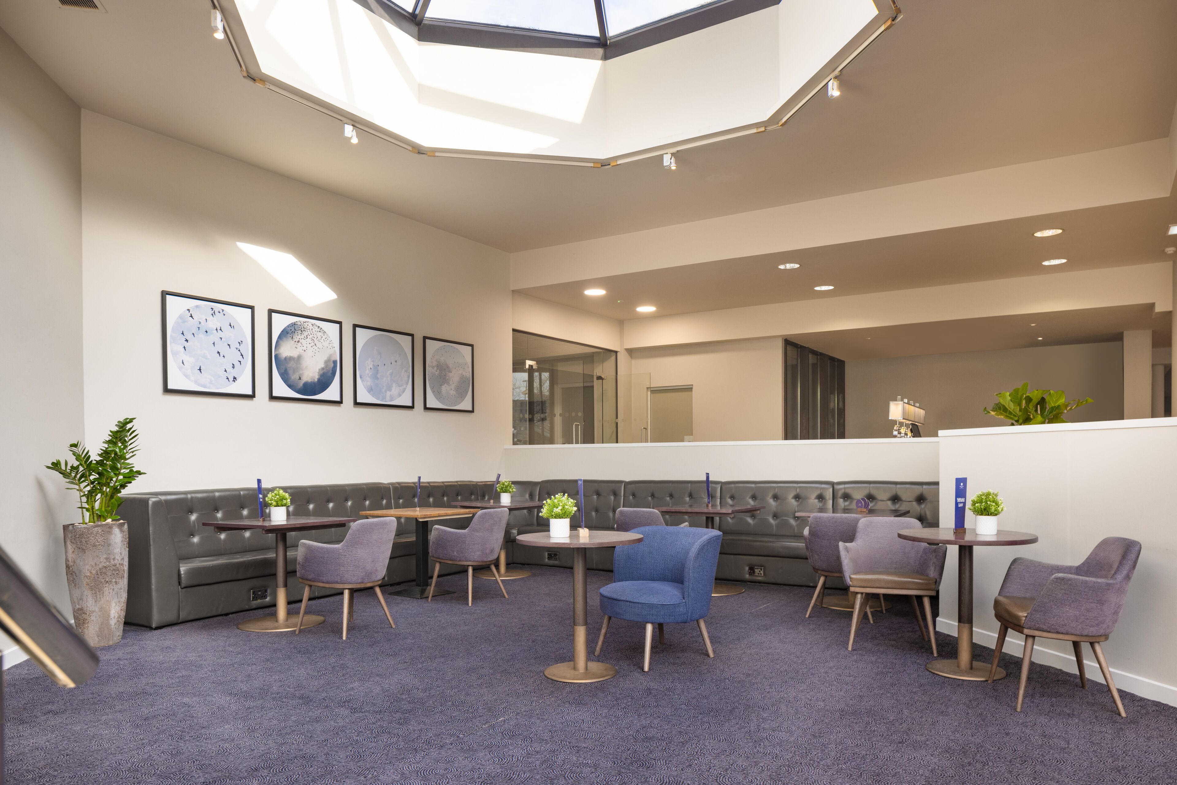 A modern lounge area with a high ceiling, seating arrangements, and artwork on the walls.