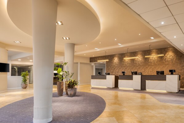 A modern reception area with a curved ceiling, a reception desk, and potted plants.