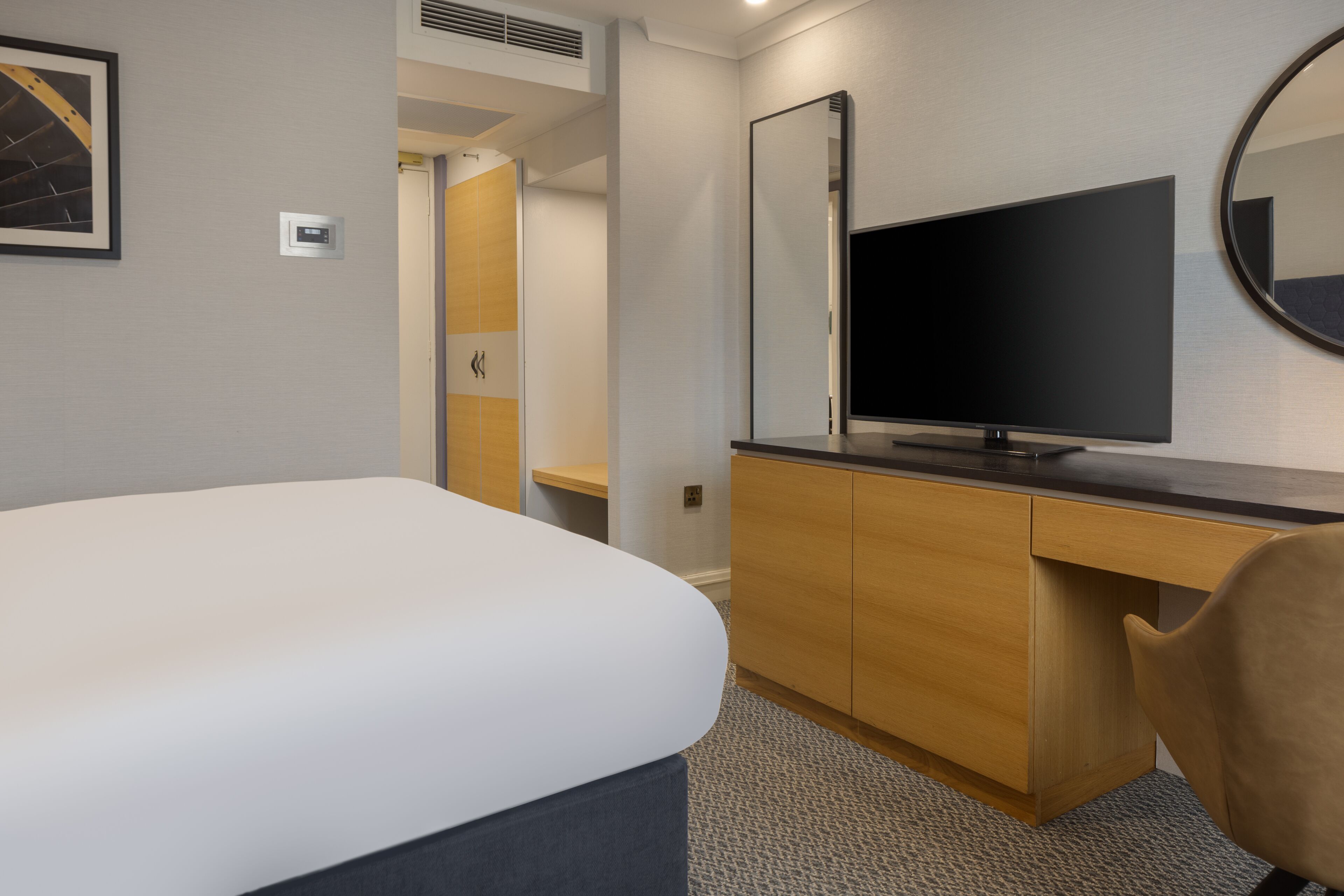 Habitación de hotel con cama, escritorio, televisor y espejo.