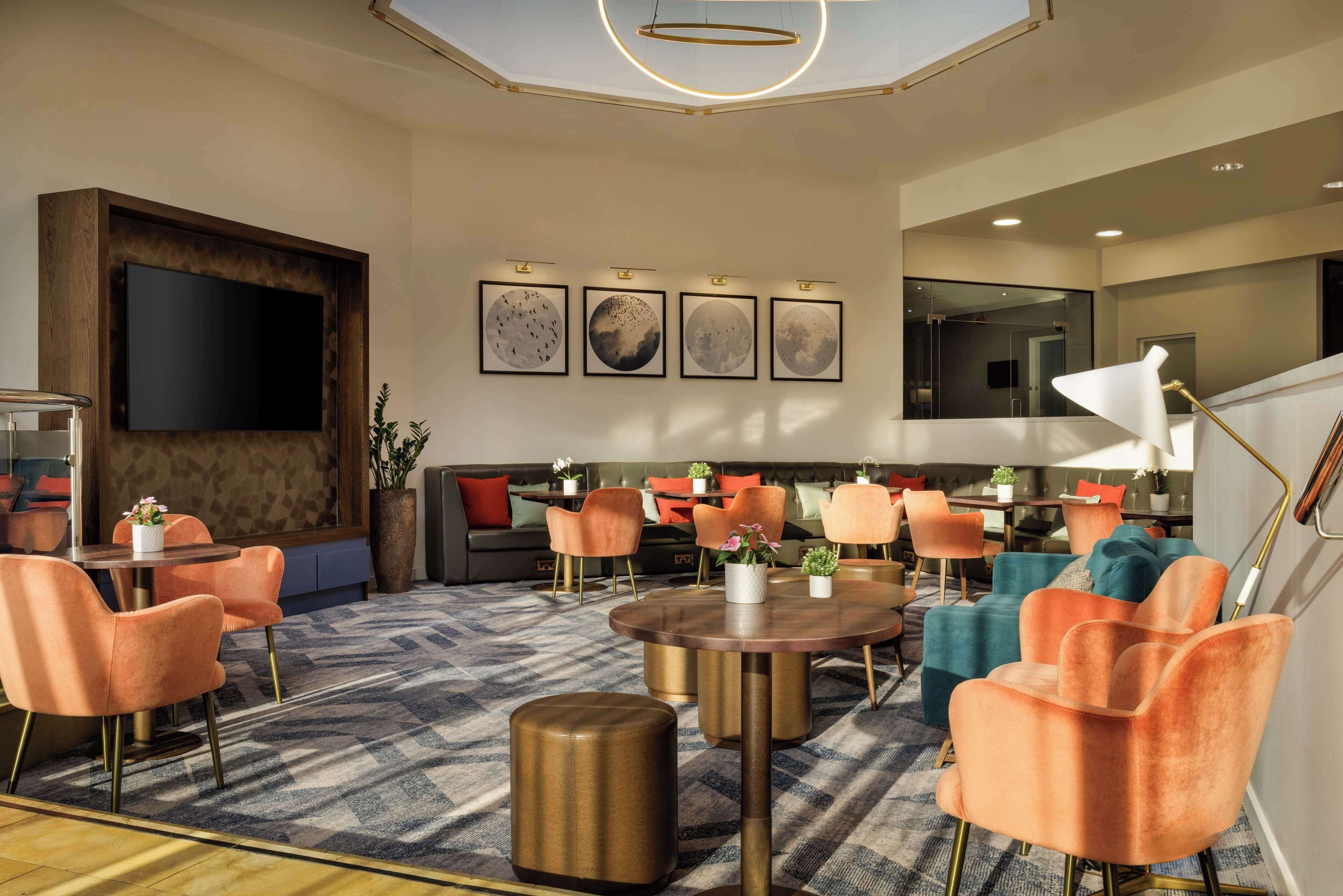 A modern hotel lobby with a large flat-screen TV, comfortable seating areas, and artwork on the walls.
