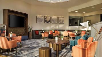 A modern hotel lobby with a large flat-screen TV, comfortable seating areas, and artwork on the walls.