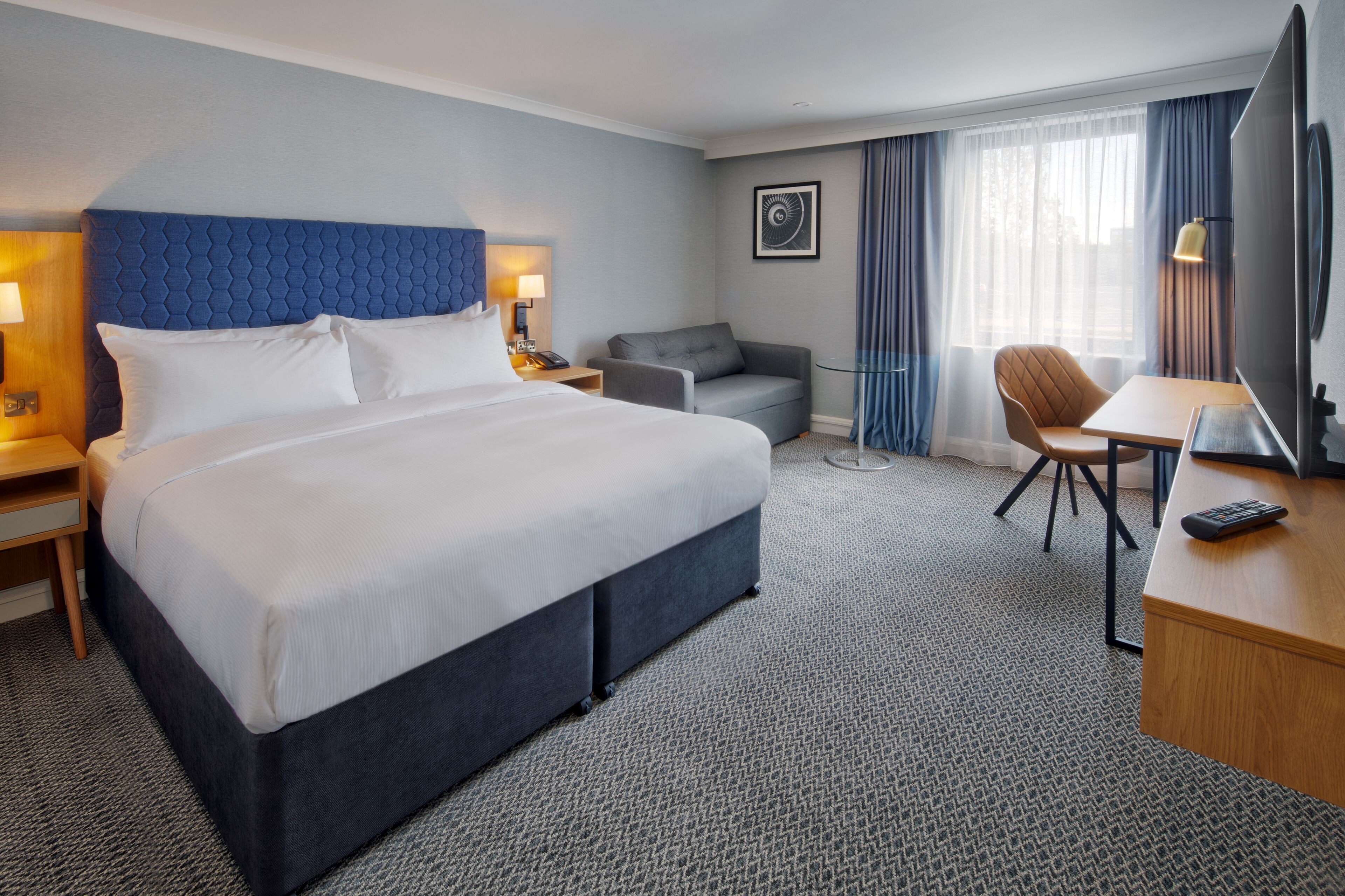 A hotel room with a large bed, a desk with a chair, a sofa, and a TV.