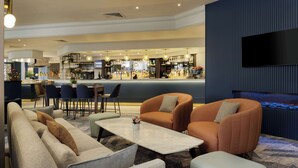 Eine moderne Hotelhalle mit Barbereich, Sitzgelegenheiten und einem an der Wand befestigten Flachbildfernseher.