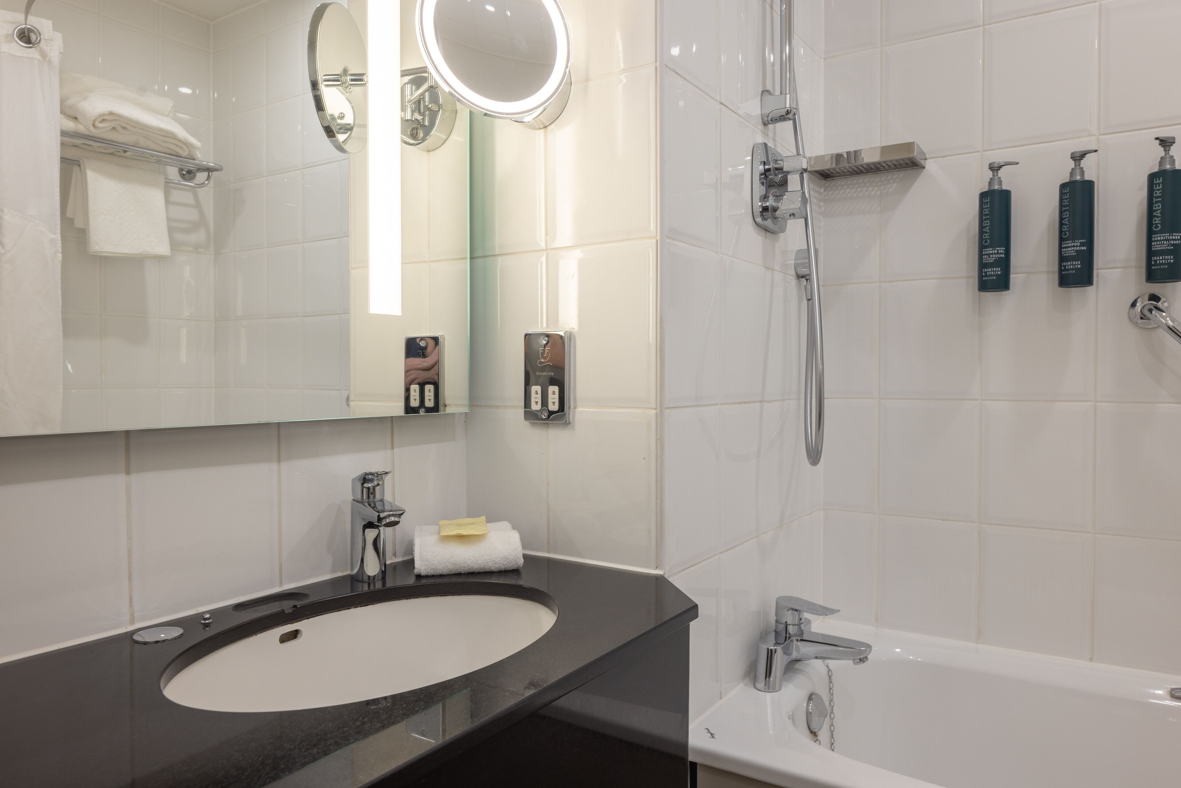 Un baño moderno con un espejo grande, un lavabo redondo, una bañera y una ducha.
