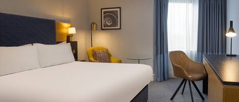 A hotel room with a large bed, a desk, a chair, a lamp, and a window with curtains.