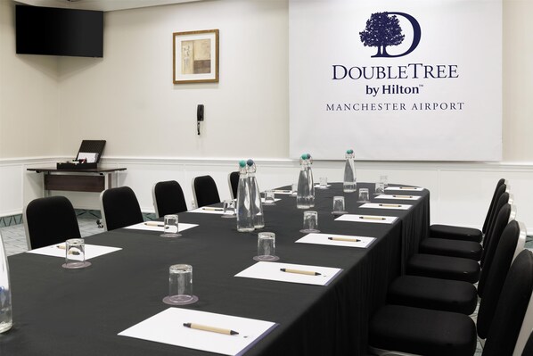 Un salón de conferencias con una larga mesa, sillas, botellas de agua y una pantalla de proyector que muestra el logotipo de DoubleTree by Hilton.