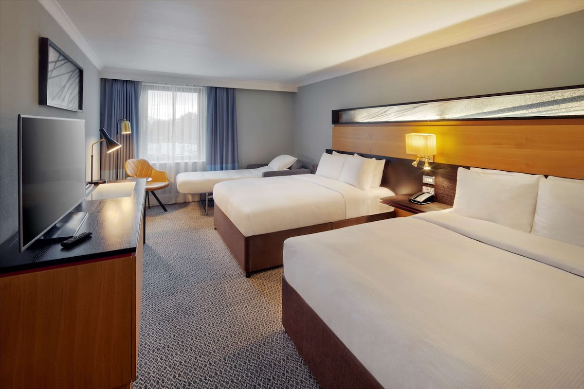 A hotel room with two beds, a desk with a TV, a chair, and a lamp.