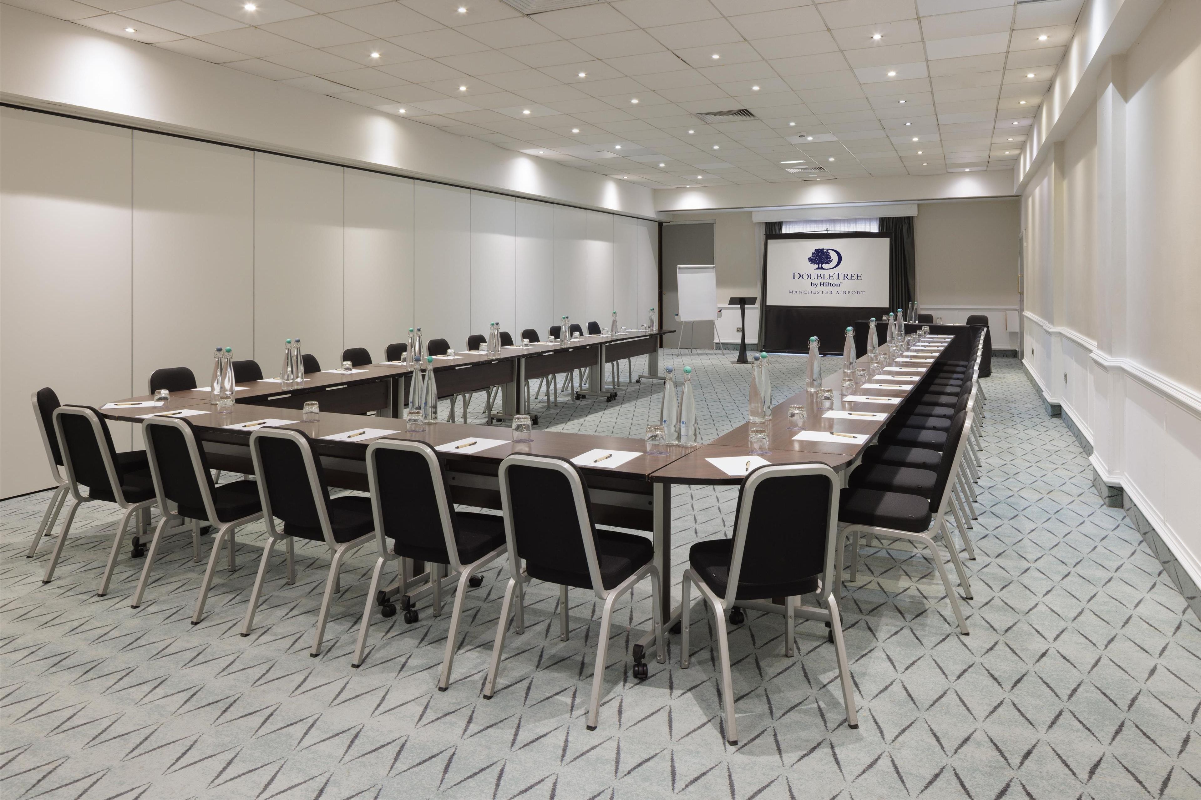 Een vergaderzaal met een lange tafel, stoelen en een presentatiescherm.