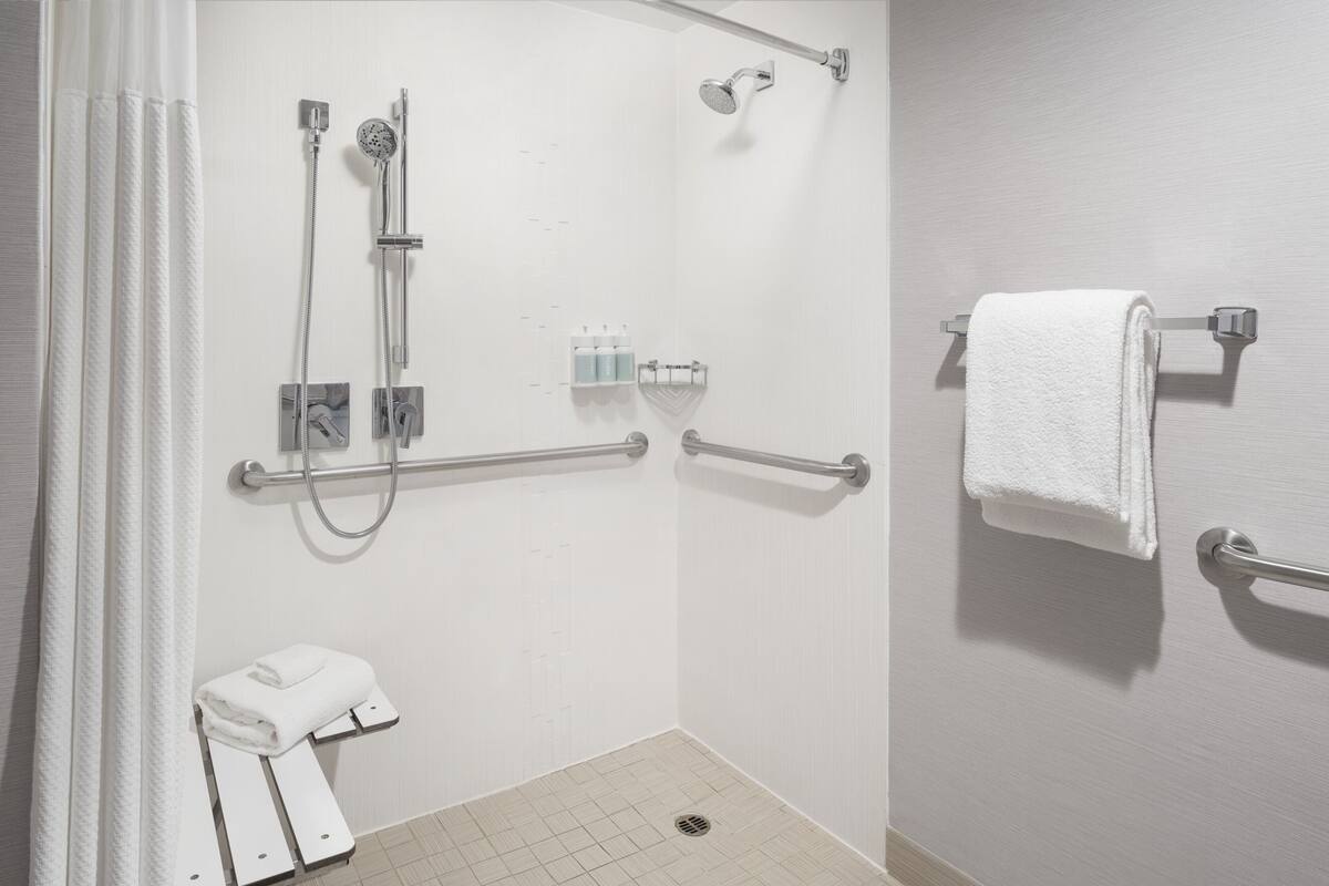 Un baño con ducha, barras de apoyo, toallero y un inodoro.