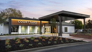 Un hotel Courtyard by Marriott con diseño moderno, que cuenta con un acceso cubierto y un jardín ajardinado.