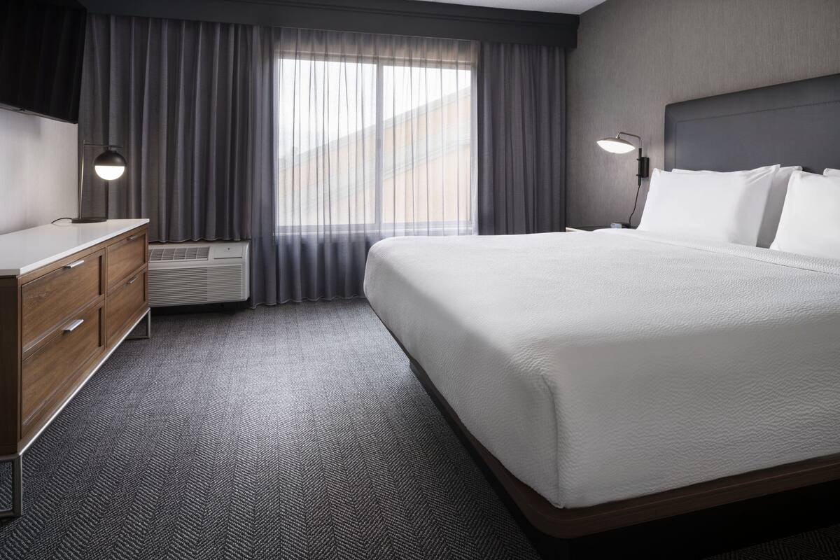 Una habitación de hotel con una cama grande, un aparador, un escritorio y una ventana con cortinas.