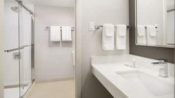 A modern bathroom with a glass-enclosed shower, a white sink with a mirror, and two white towels hanging on the wall.