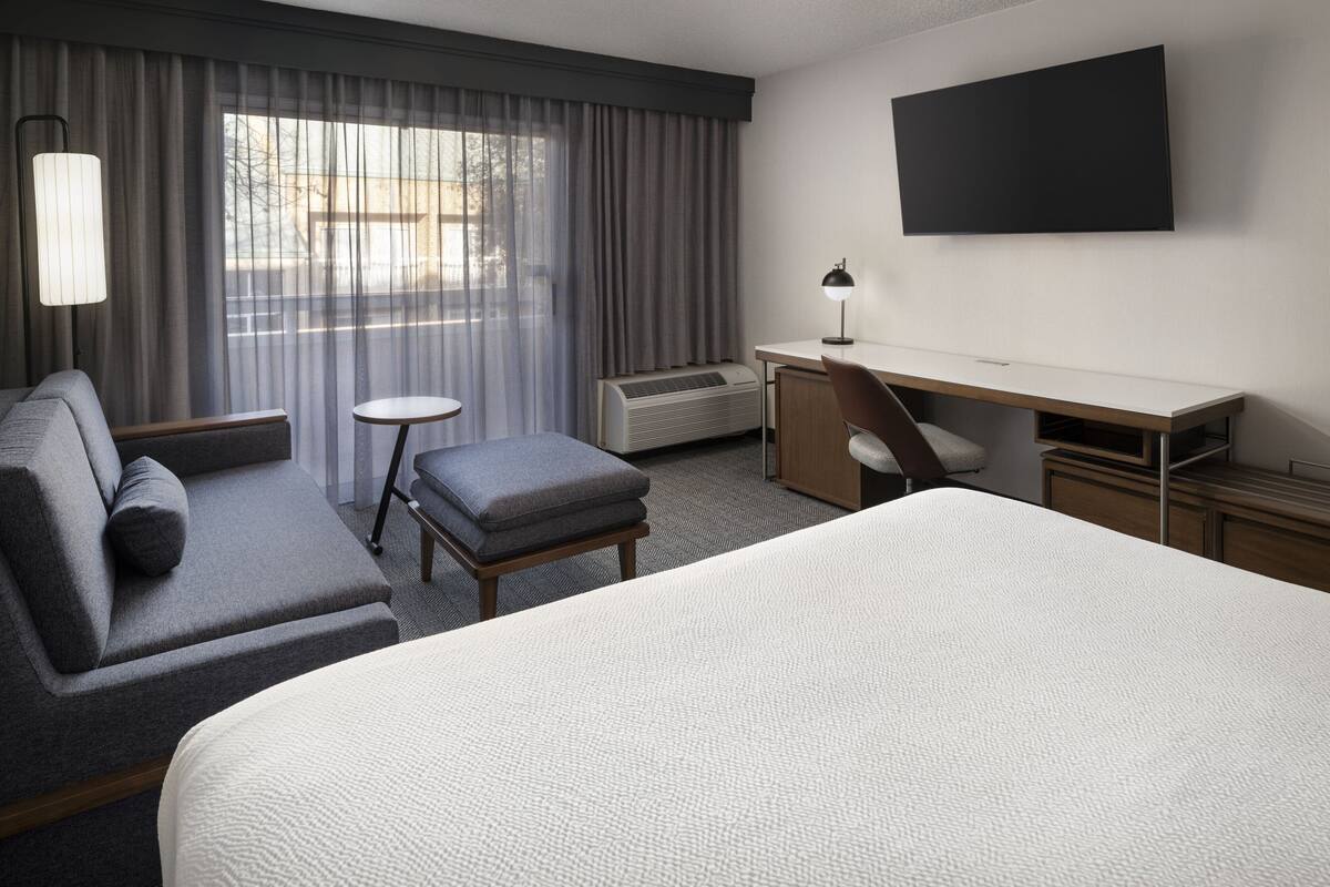 Una habitación de hotel con una cama grande, un escritorio, una silla, una mesita y un televisor.
