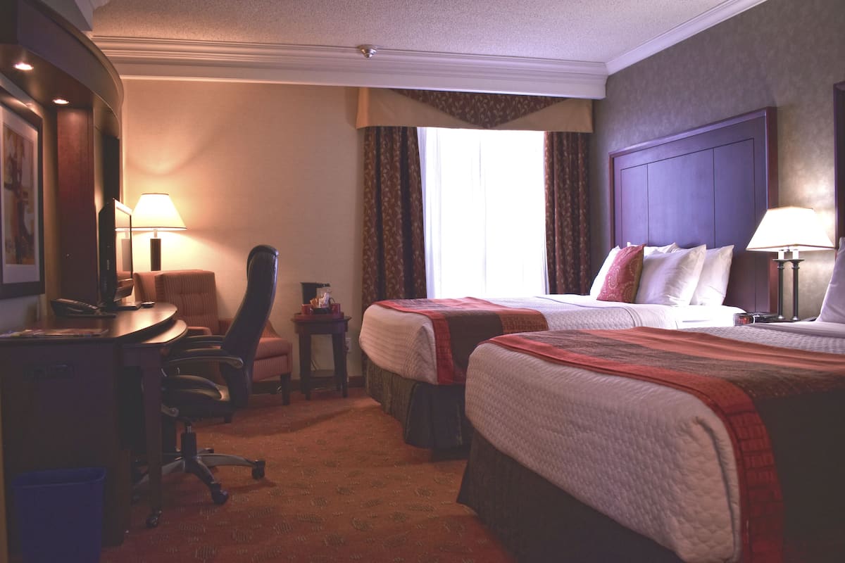 A hotel room with two beds, a desk, a chair, a small table, and a window with curtains.