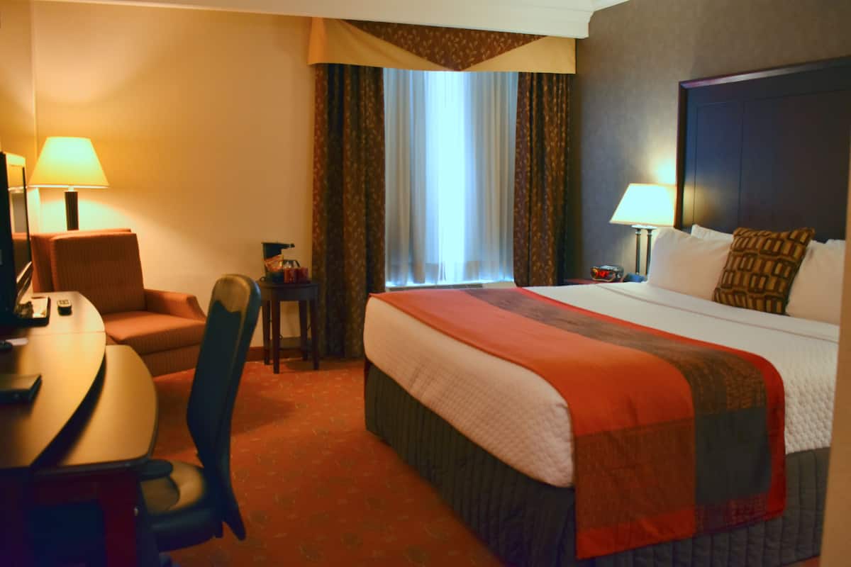 A hotel room with a bed, a desk, a chair, a lamp, and a window with curtains.