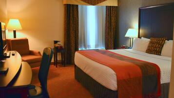 A hotel room with a bed, a desk, a chair, a lamp, and a window with curtains.