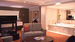 Een hotelkamer met een zithoek, inclusief een bank, een salontafel met tijdschriften, een open haard en een televisie.