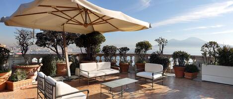 Una terraza en la azotea con muebles de exterior, un parasol grande y plantas en macetas.