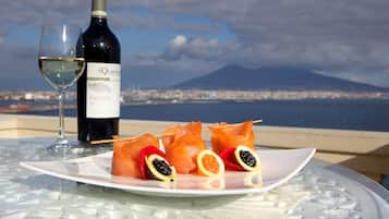 Una copa de vino blanco, una botella de vino y un plato con salmón y cítricos sobre una mesa con superficie de vidrio, con vista a una ciudad y una montaña.