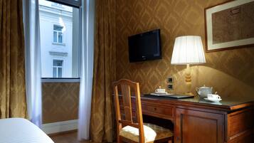 A hotel room with a bed, a desk with a lamp, a chair, a television, and a window with curtains.