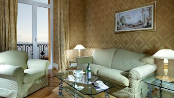 A room with a sofa, armchairs, a glass coffee table, and a painting on the wall.