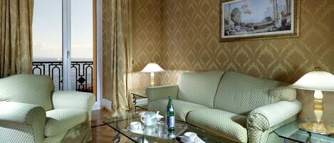 A room with a sofa, armchairs, a glass coffee table, and a painting on the wall.