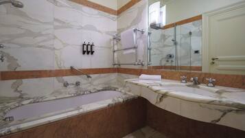 A bathroom with a marble wall, a bathtub, a shower, and a vanity with two sinks.