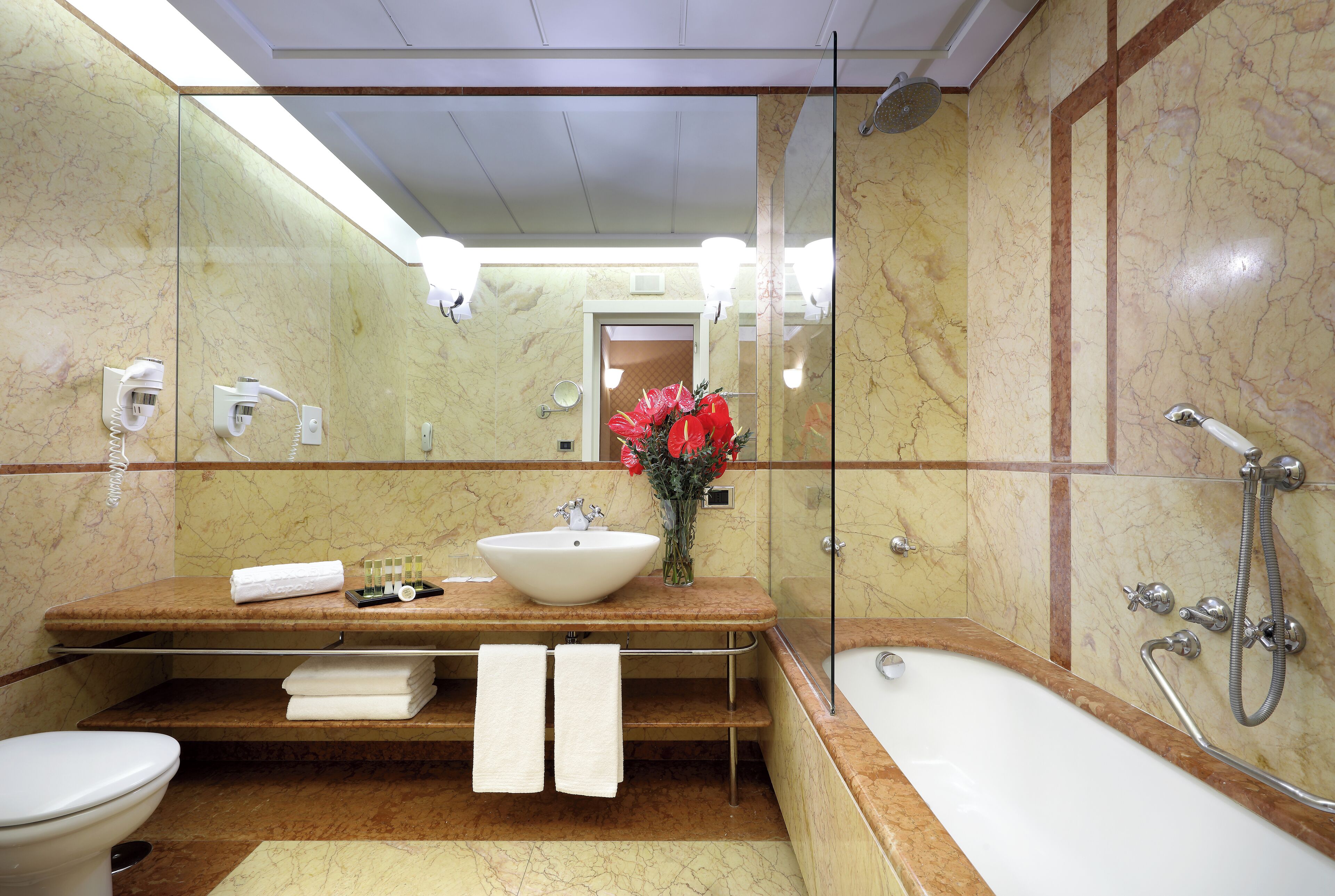 Une salle de bain avec un lavabo en marbre, une baignoire et une douche. Il y a des serviettes sur le comptoir et un vase avec des fleurs.