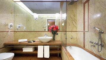 Une salle de bain avec un lavabo en marbre, une baignoire et une douche. Il y a des serviettes sur le comptoir et un vase avec des fleurs.