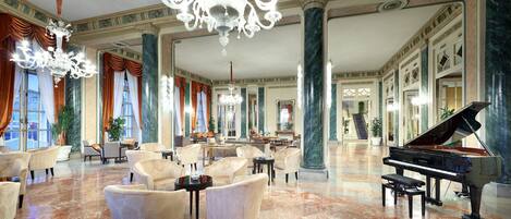 Un vestíbulo amplio con un piano de cola, elegantes candelabros y zonas de estar confortables.