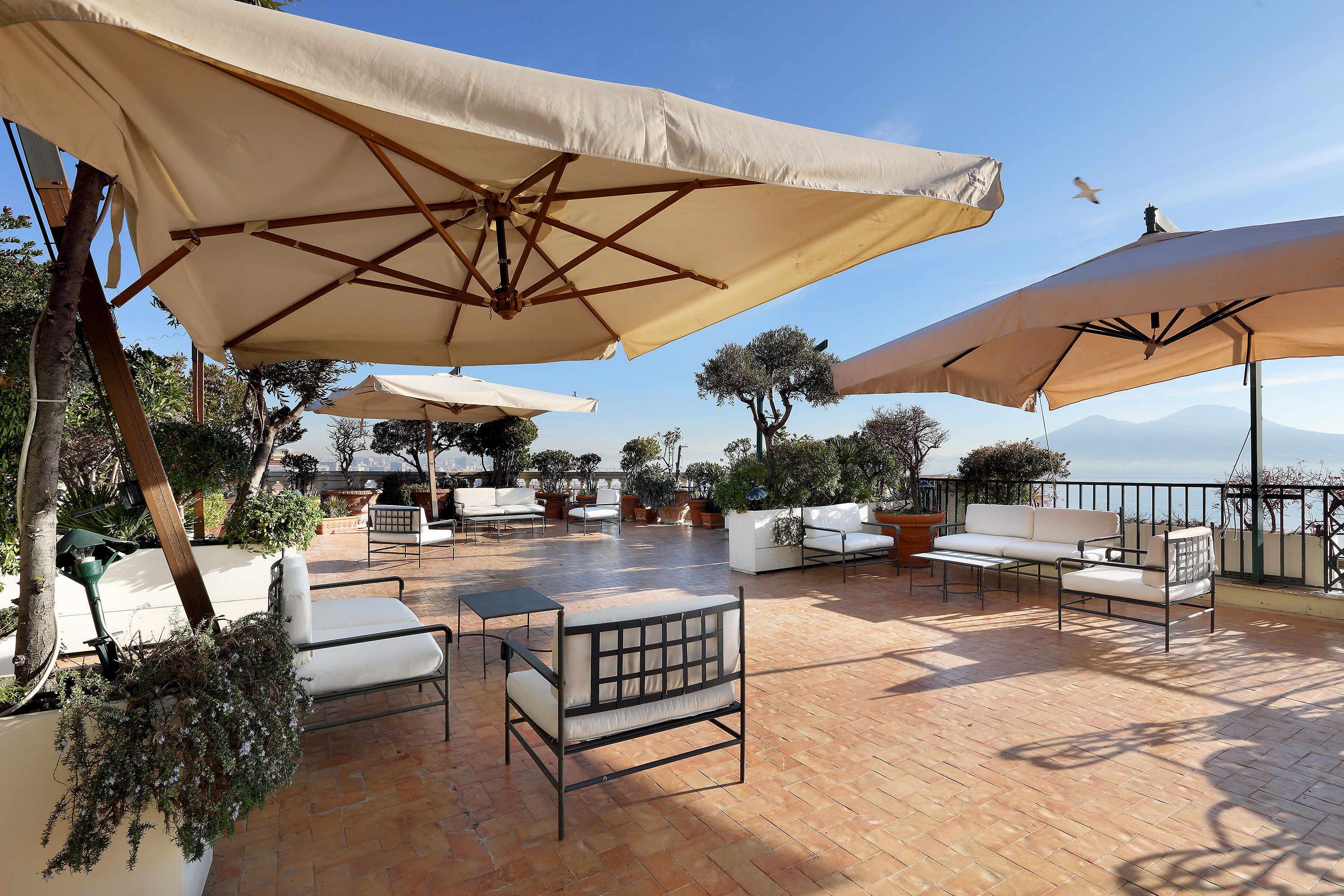 Una terrazza con posti a sedere all'aperto, ombrelloni e vasi di piante.