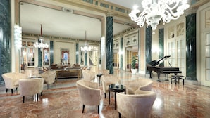 A spacious lobby with marble flooring, multiple seating areas, a grand piano, and a chandelier. - Eurostars Hotel Excelsior (Naples)