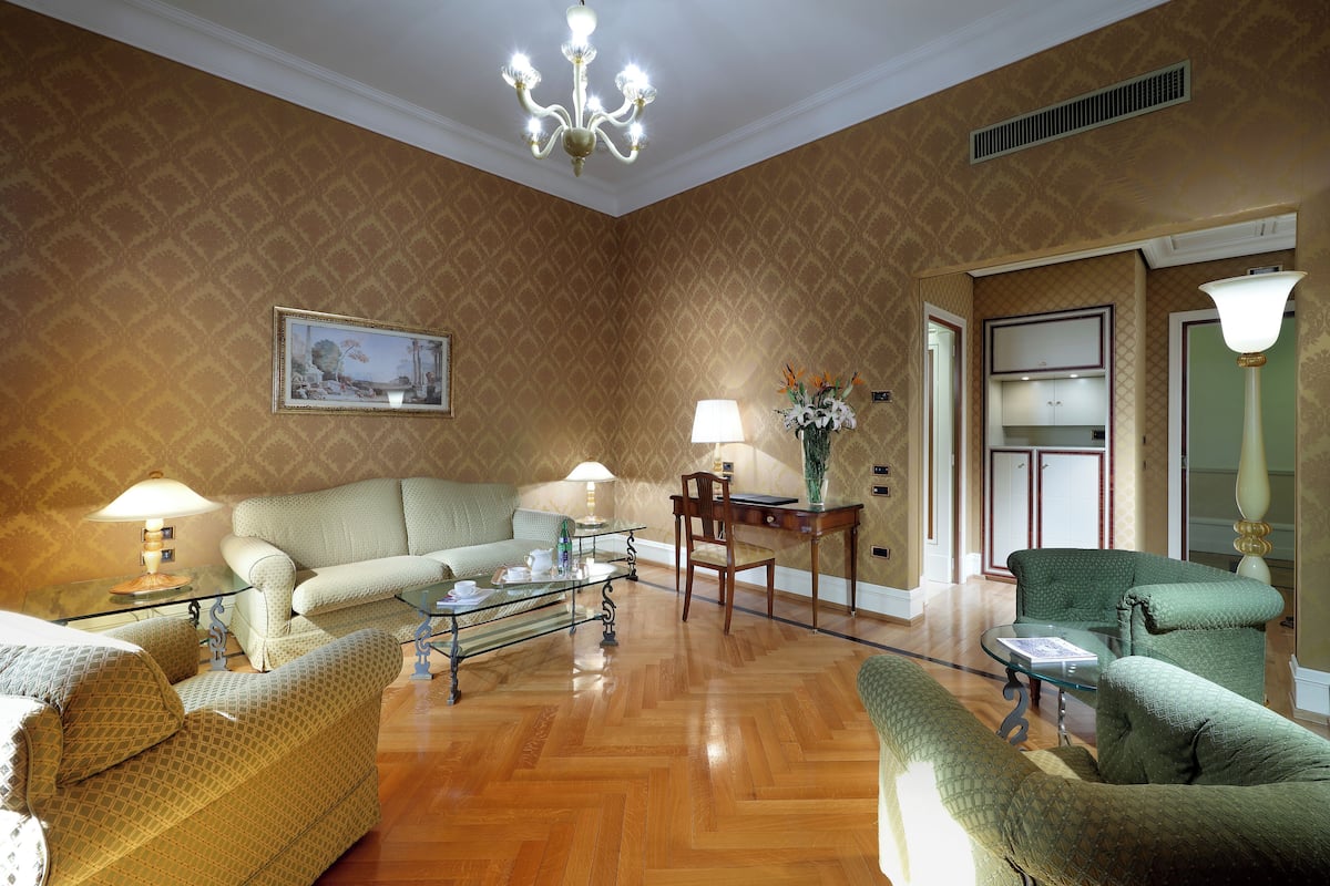 A spacious living room with a wooden floor, a green sofa, a glass coffee table, and a chandelier.