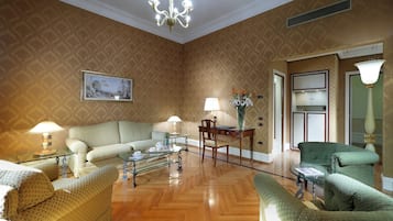 A spacious living room with a wooden floor, a green sofa, a glass coffee table, and a chandelier.