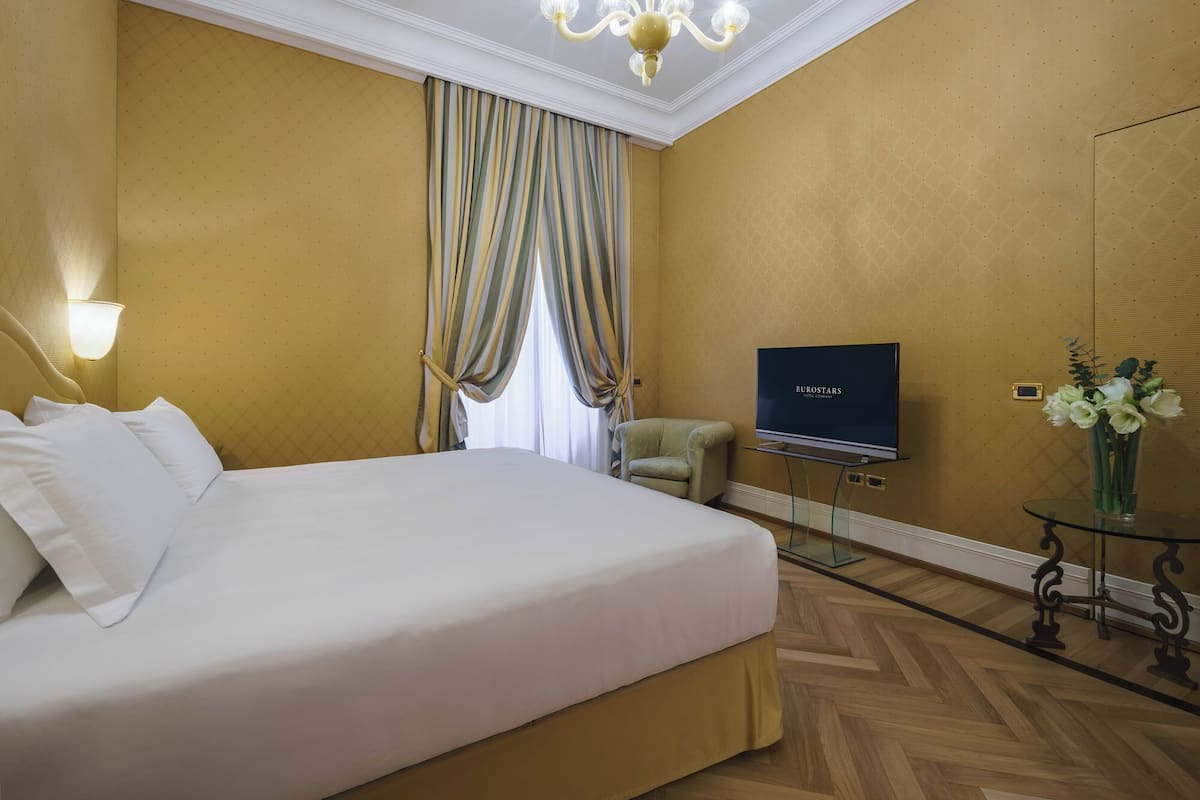 A hotel room with a large bed, a television, a chair, and a vase with flowers.