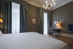 Una camera d'albergo con un letto grande, un lampadario, una scrivania con lampada e una televisione.