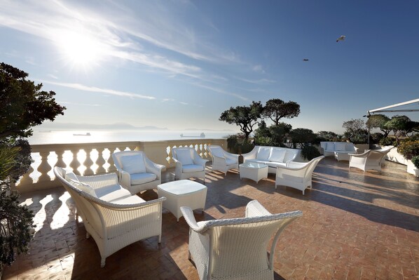 An outdoor patio with wicker furniture and a view of the sea. - Eurostars Hotel Excelsior (Naples)