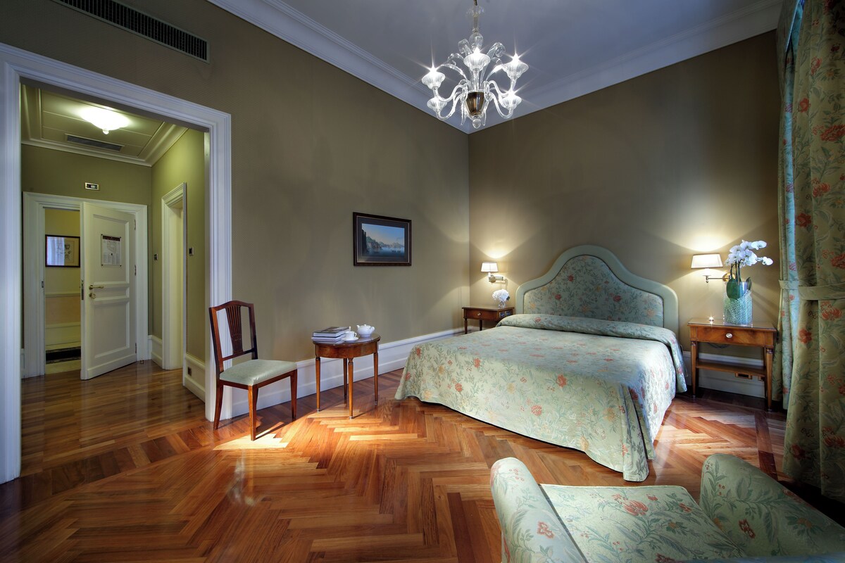 A bedroom with a large bed, two bedside tables, a chair, and a chandelier.