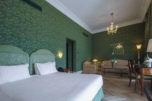Een hotelkamer met een groot bed, twee stoelen, een bank, een bureau met een lamp en een kroonluchter.